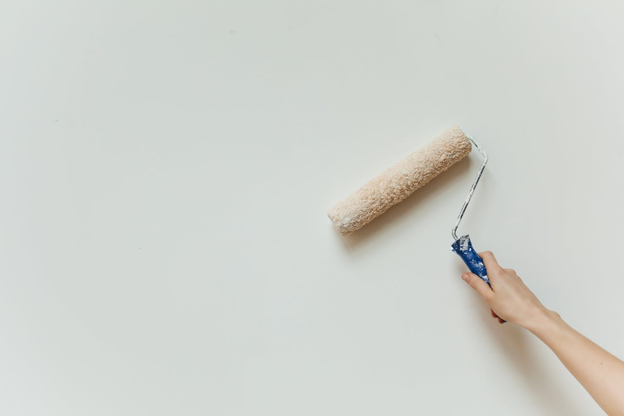 Close-up of a hand painting a wall with a roller brush during renovation.
